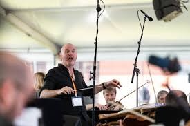 Julian Ferraretto conducting a string ensemble at an outdoor festival